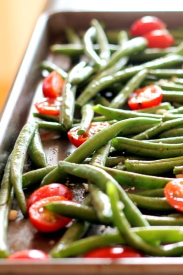 Roasted garlic parmesan green beans with tomatoes on a baking tray