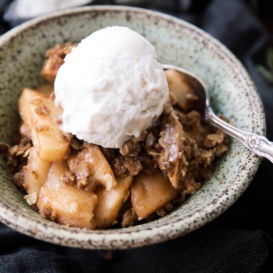 Maple pecan apple crisp in a bowl topped with ice cream