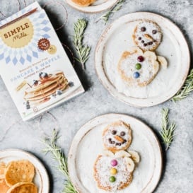 Grain free snowman pancakes on plates next to a box of pancake mix