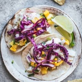 two fish tacos on a plate topped with mango salsa and cabbage slaw
