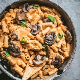 sweet potato penne pasta with vegan sweet potato cream sauce in a skillet with mushrooms and a wooden spoon