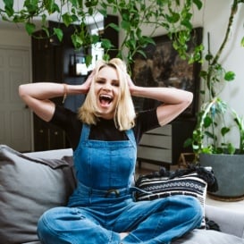 blonde woman in overalls sitting on a soft grey chair