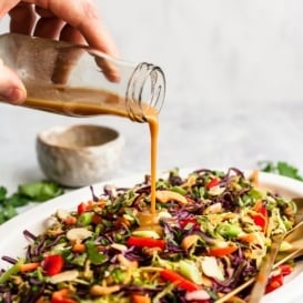 pouring sesame ginger dressing onto a salad