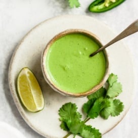 jalapeno green tahini sauce in a bowl with a spoon and garnishes on the side