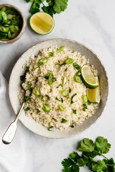 cauliflower rice in a bowl with scallions and limes