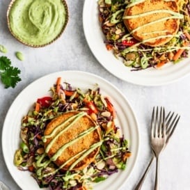 two sweet potato salmon cakes on two plates with salad and green dressing on the side