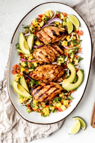 chicken breasts on a platter with avocado slices, red onion, and pico de gallo