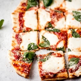 grilled pizza with cheese, tomato sauce, and basil cut into 16 squares