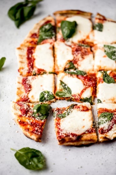 grilled pizza with cheese, tomato sauce, and basil cut into 16 squares
