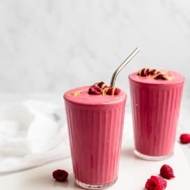 two peanut butter and jelly smoothies in glasses topped with raspberries and peanut butter
