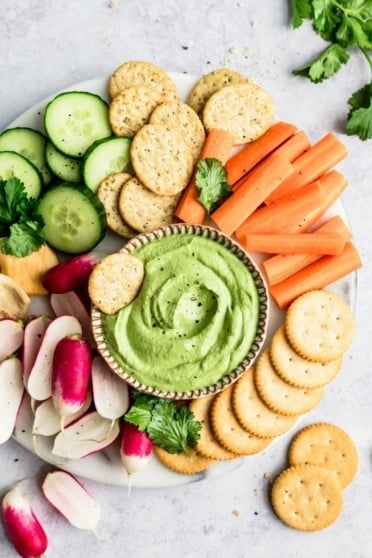spicy green cashew dip on a platter with veggies and crackers