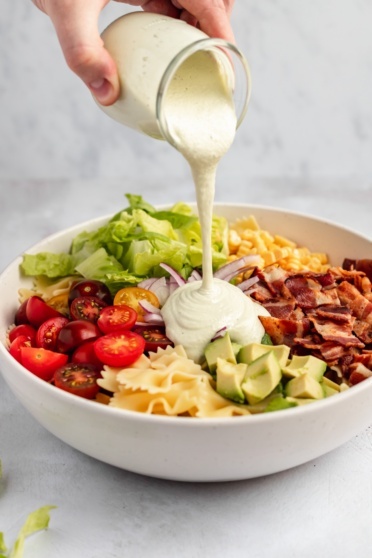 pouring vegan cashew cream sauce into a pasta salad