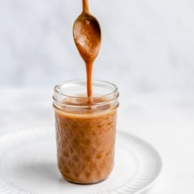 spooning vegan peanut butter caramel sauce out of a jar