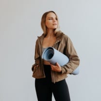 woman holding a yoga mat in an olive jacket