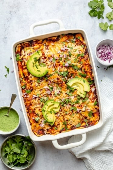 chicken enchiladas in a pan topped with avocado