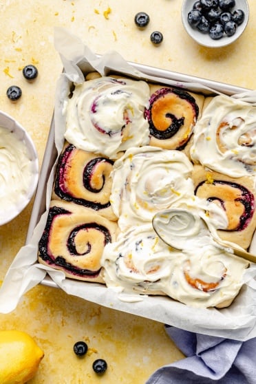 spreading lemon cream cheese frosting onto lemon blueberry sweet rolls