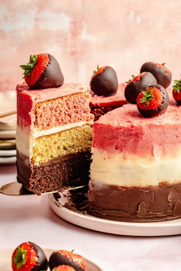 a slice of Neapolitan cake with chocolate covered strawberries on top