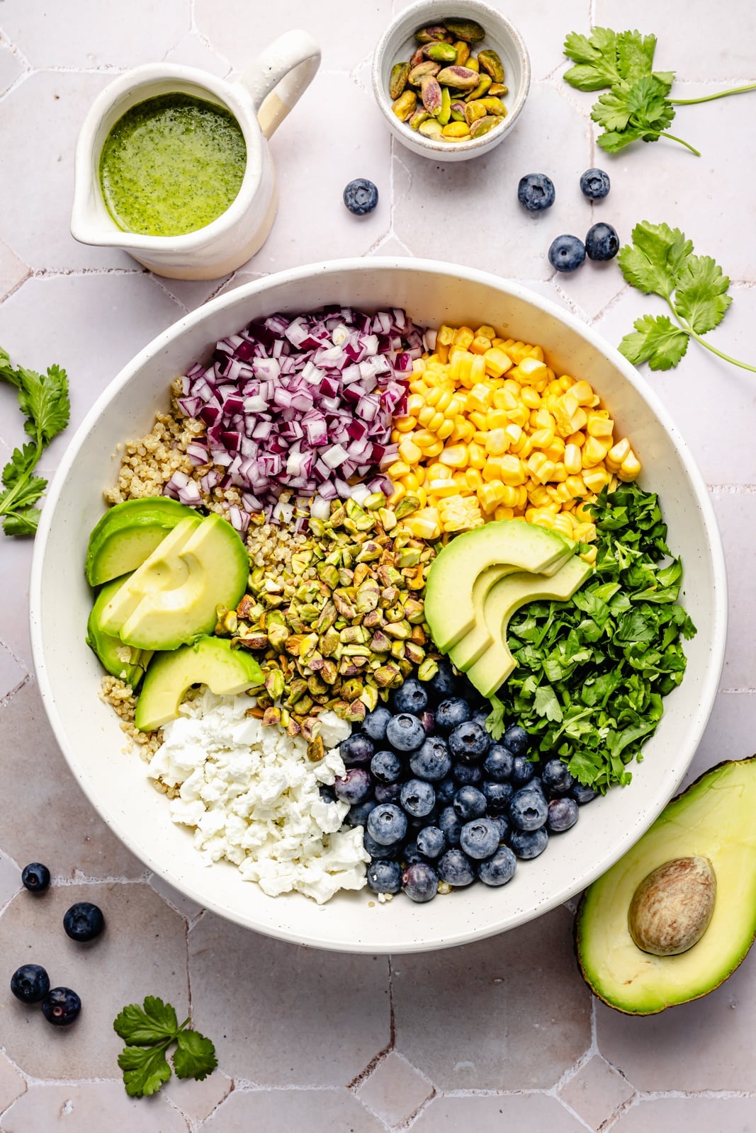 Beautiful avocado blueberry quinoa salad loaded with fresh produce, tangy feta, chopped pistachios, and tossed in a flavorful cilantro lime dressing. This delicious quinoa salad is packed with plant-based protein and is perfect for summer lunches, parties, and picnics. unmixed avocado blueberry quinoa salad in a bowl