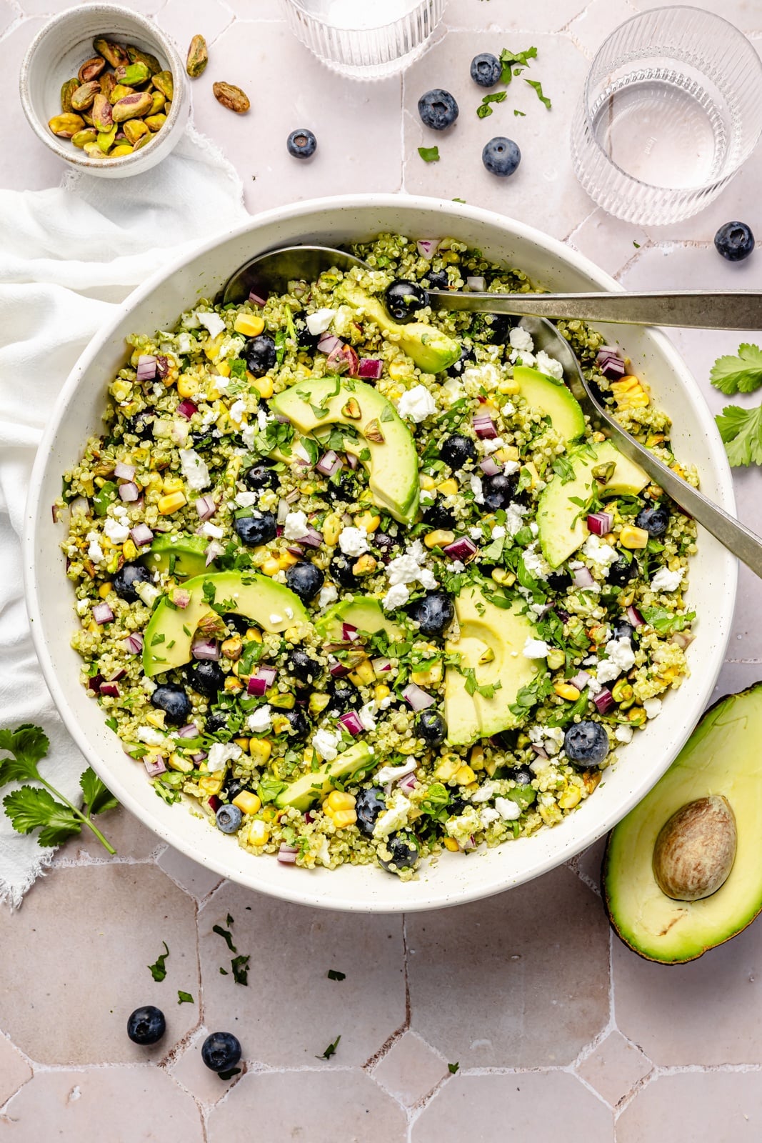 Beautiful avocado blueberry quinoa salad loaded with fresh produce, tangy feta, chopped pistachios, and tossed in a flavorful cilantro lime dressing. This delicious quinoa salad is packed with plant-based protein and is perfect for summer lunches, parties, and picnics. avocado blueberry quinoa salad in a large bowl with serving spoons