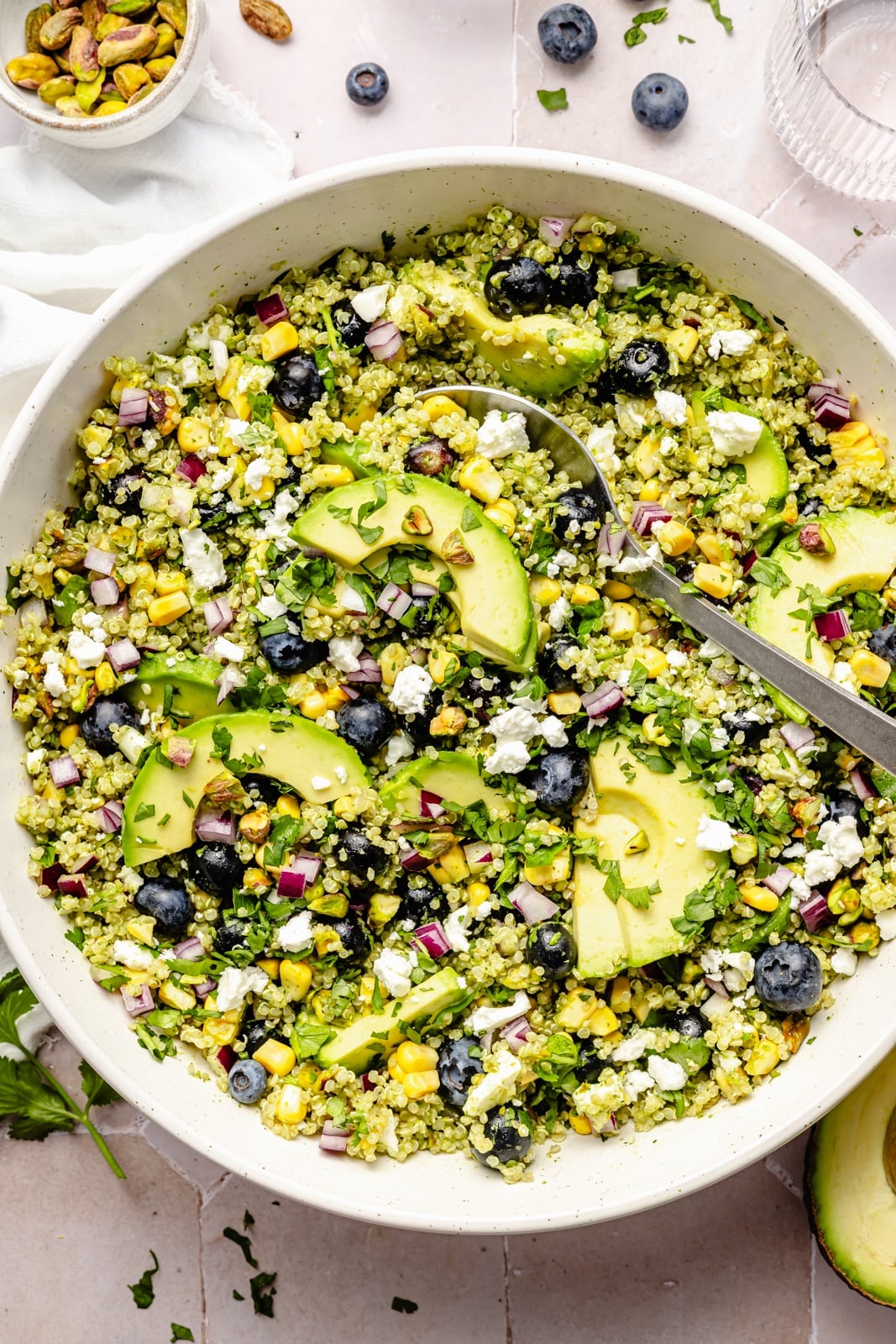 Beautiful avocado blueberry quinoa salad loaded with fresh produce, tangy feta, chopped pistachios, and tossed in a flavorful cilantro lime dressing. This delicious quinoa salad is packed with plant-based protein and is perfect for summer lunches, parties, and picnics. blueberry quinoa salad with avocado in a large bowl