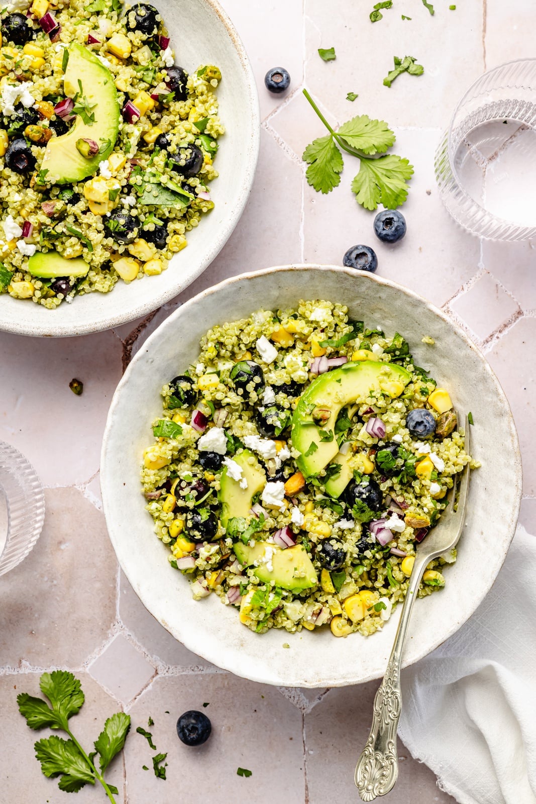 Beautiful avocado blueberry quinoa salad loaded with fresh produce, tangy feta, chopped pistachios, and tossed in a flavorful cilantro lime dressing. This delicious quinoa salad is packed with plant-based protein and is perfect for summer lunches, parties, and picnics. healthy blueberry quinoa salad in two bowls