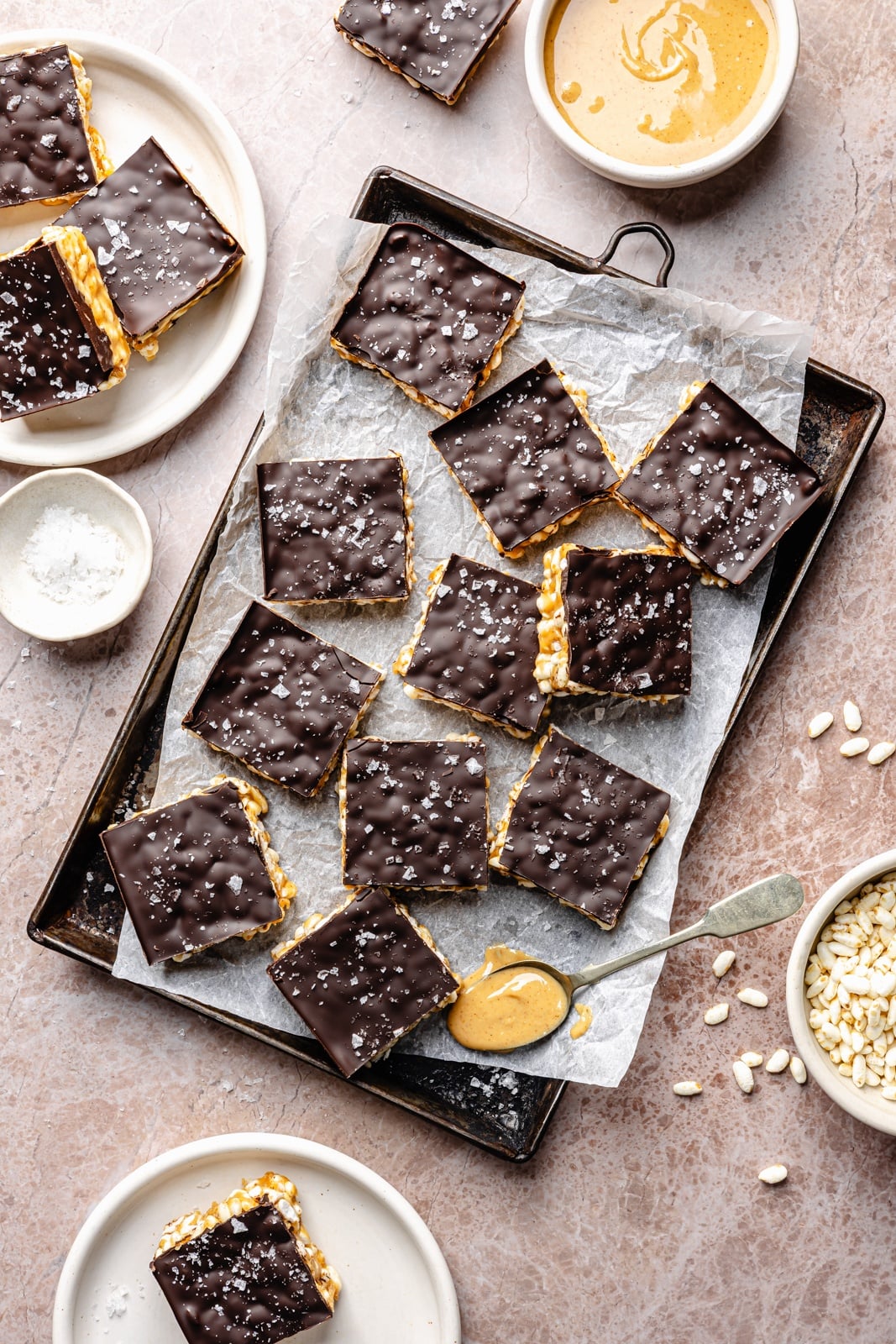 Healthy rice krispie treats made without marshmallows and with peanut butter, coconut oil, maple syrup, and brown rice krispies. These vegan and gluten-free peanut butter rice krispie treats are topped with dark chocolate and sea salt for an indulgent treat that tastes just like a crunchy peanut butter cup. Options to add a bit of protein powder to make these a great post-workout treat! healthy peanut butter rice krispie treats on parchment paper