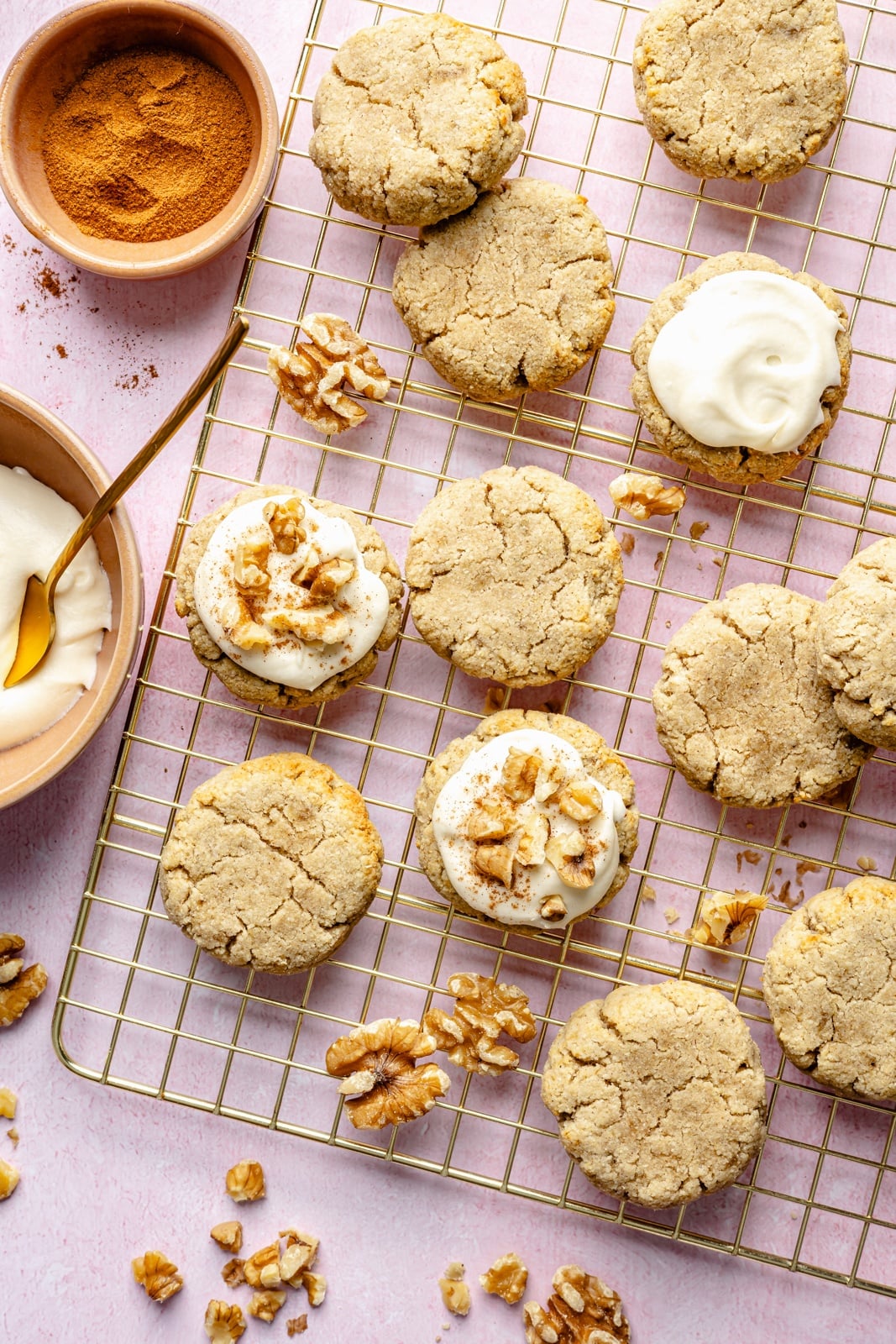 Soft, healthy banana cookies made with a mix of almond and coconut flour to make them gluten and grain-free! These banana bread cookies taste like a slice of your favorite banana bread and are topped with a luscious cream cheese frosting for a delicious treat everyone loves. topping banana cookies with frosting on a wire rack