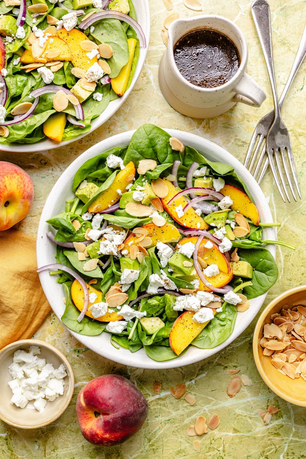 peach spinach salad in bowls next to a jar of balsamic dressing