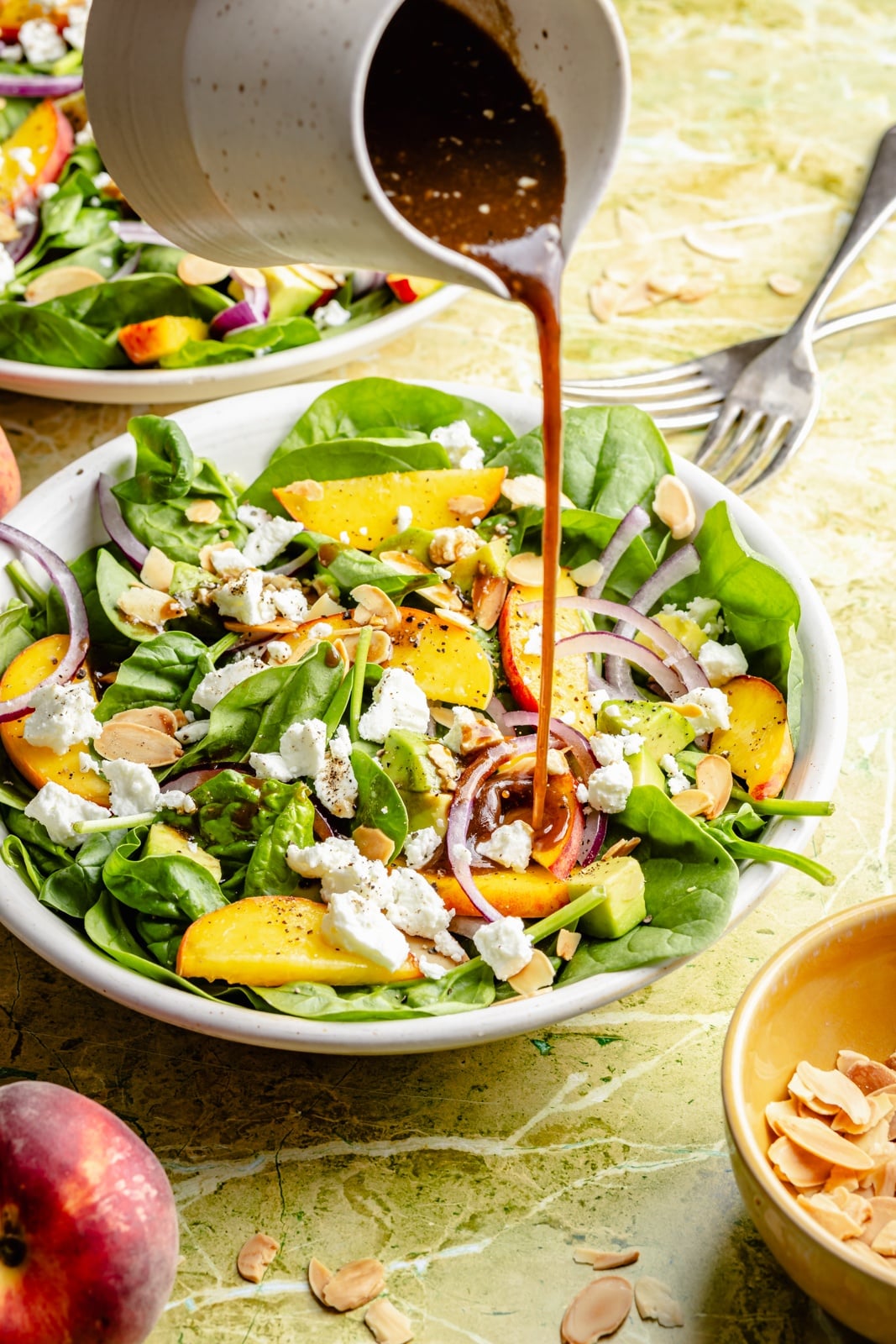 pouring balsamic over a peach salad with spinach