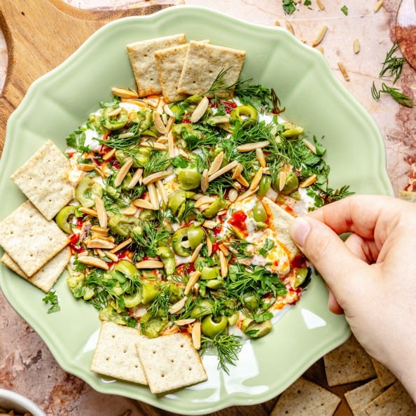 dipping a cracker into whipped goat cheese yogurt dip with olives