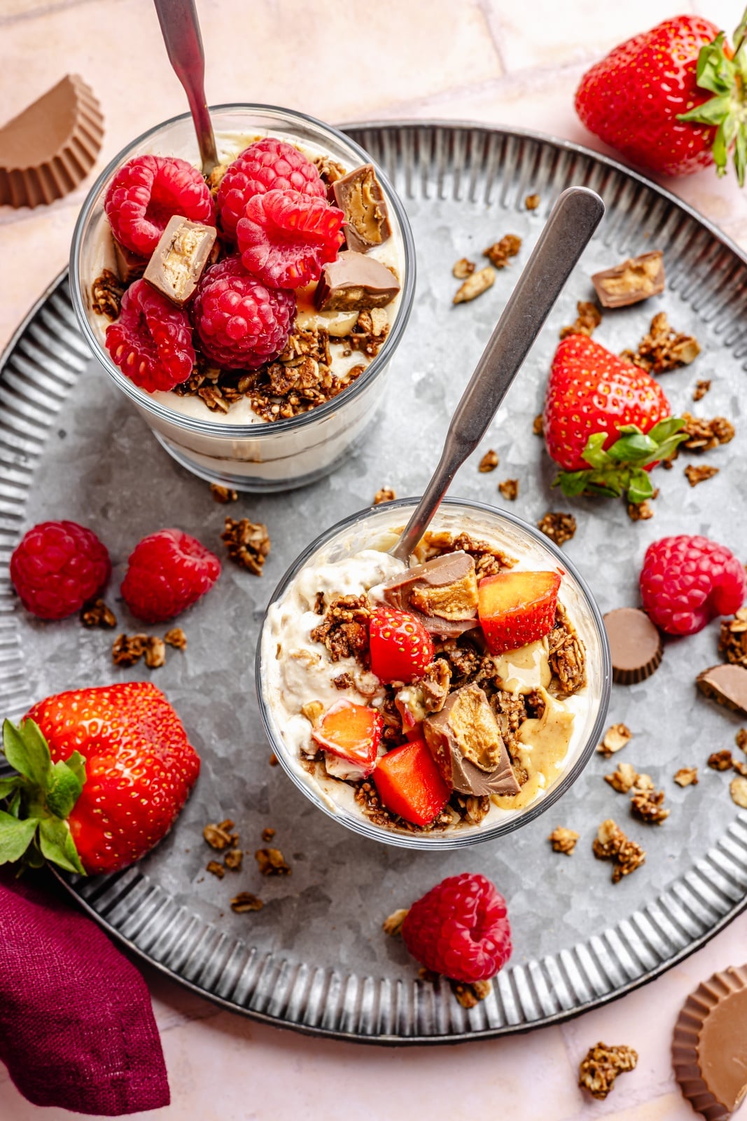 Creamy, high-protein peanut butter cup cheesecake jars layered with crunchy chocolate granola. Top these jars with fresh berries for a healthy breakfast or snack, and add chopped peanut butter cups for a more indulgent dessert! They take just 15 minutes to make and pack over 20g of protein from cottage cheese and greek yogurt. top-down view of two healthy peanut butter cup cheesecake jars