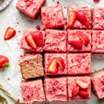 strawberry snacking cake with strawberry frosting sliced on parchment paper