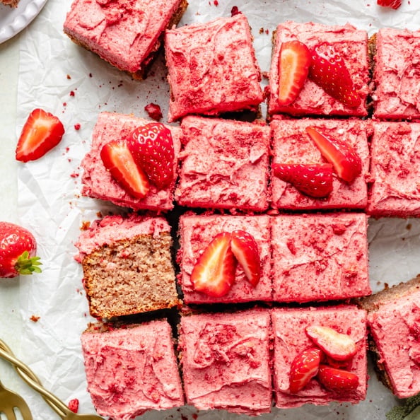 strawberry snacking cake with strawberry frosting sliced on parchment paper