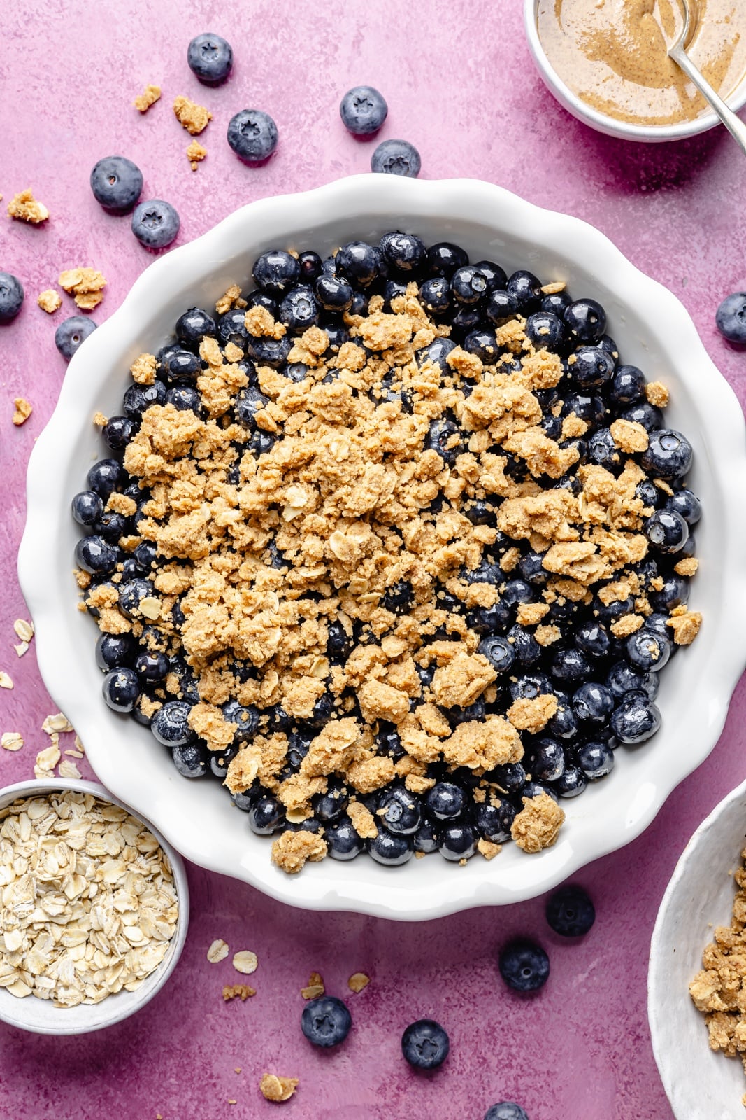 Golden, bubbly blueberry crisp with a perfectly sweet almond butter crumble. This delicious blueberry crisp recipe is easily made gluten-free, dairy-free, and vegan, and makes the perfect summer dessert for sharing. Add a scoop of vanilla ice cream and a drizzle of extra almond butter for good measure! assembling a gluten-free blueberry crisp in a baking pan