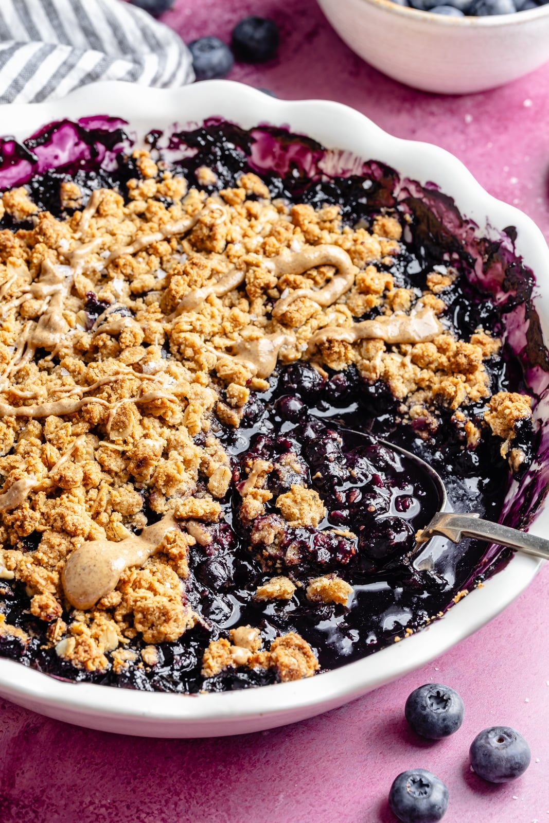 Golden, bubbly blueberry crisp with a perfectly sweet almond butter crumble. This delicious blueberry crisp recipe is easily made gluten-free, dairy-free, and vegan, and makes the perfect summer dessert for sharing. Add a scoop of vanilla ice cream and a drizzle of extra almond butter for good measure! blueberry crisp with almond butter crumble in a baking pan with a spoon