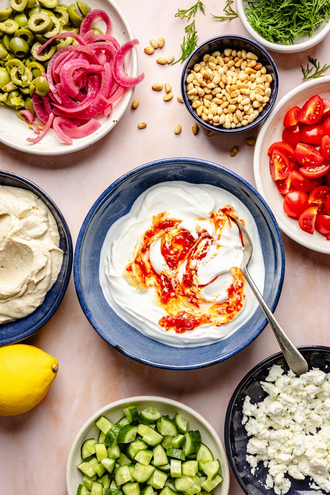 Easy, flavorful Mediterranean dip layered with hummus, creamy yogurt, and fresh toppings like olives, cucumber, and feta cheese. This savory party appetizer is a fun take on classic 7-layer dip and is delicious served with pita chips, pretzels, or naan bread! ingredients for layered mediterranean dip in bowls