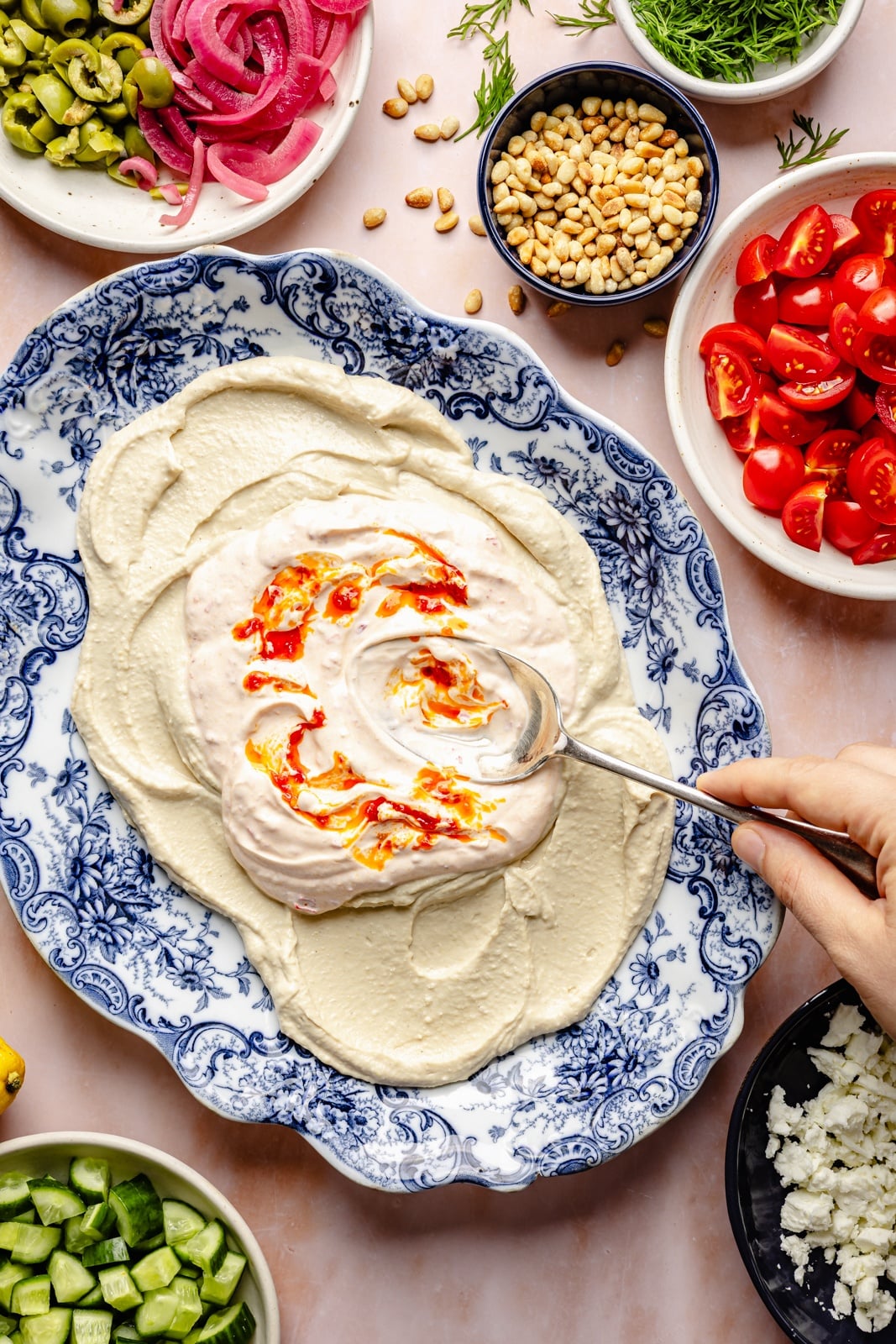 Easy, flavorful Mediterranean dip layered with hummus, creamy yogurt, and fresh toppings like olives, cucumber, and feta cheese. This savory party appetizer is a fun take on classic 7-layer dip and is delicious served with pita chips, pretzels, or naan bread! layering yogurt on top of hummus to make a layered mediterranean dip on a platter
