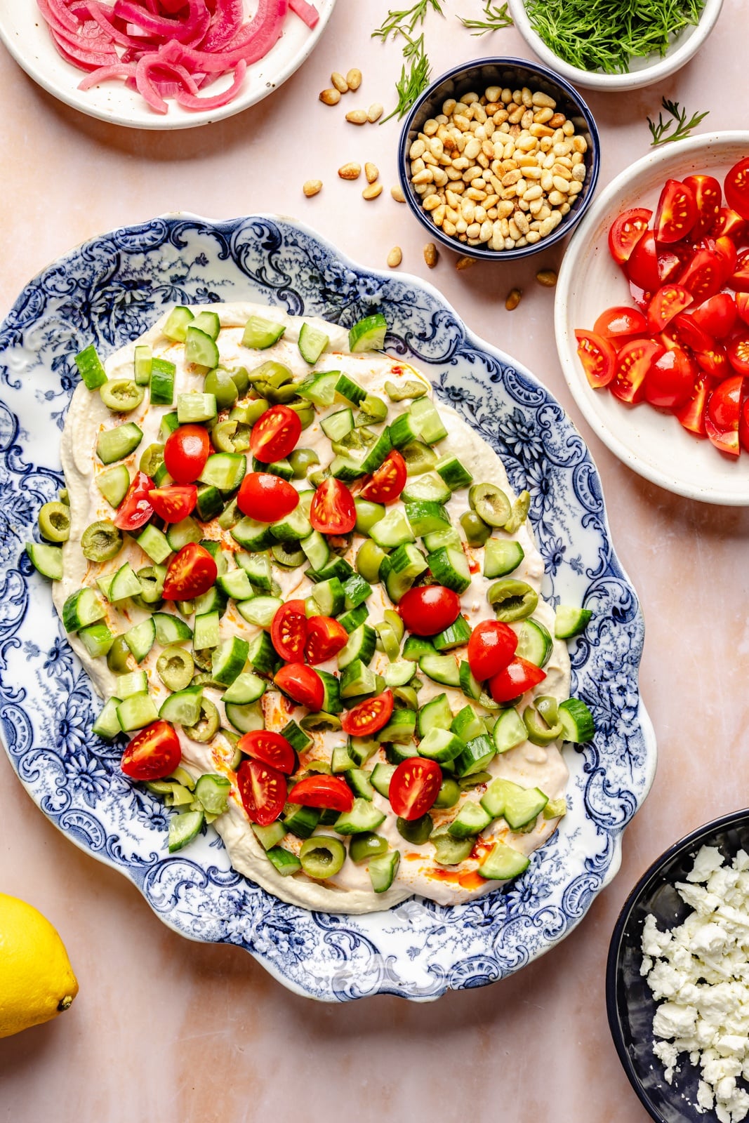 Easy, flavorful Mediterranean dip layered with hummus, creamy yogurt, and fresh toppings like olives, cucumber, and feta cheese. This savory party appetizer is a fun take on classic 7-layer dip and is delicious served with pita chips, pretzels, or naan bread! mediterranean dip on a blue platter