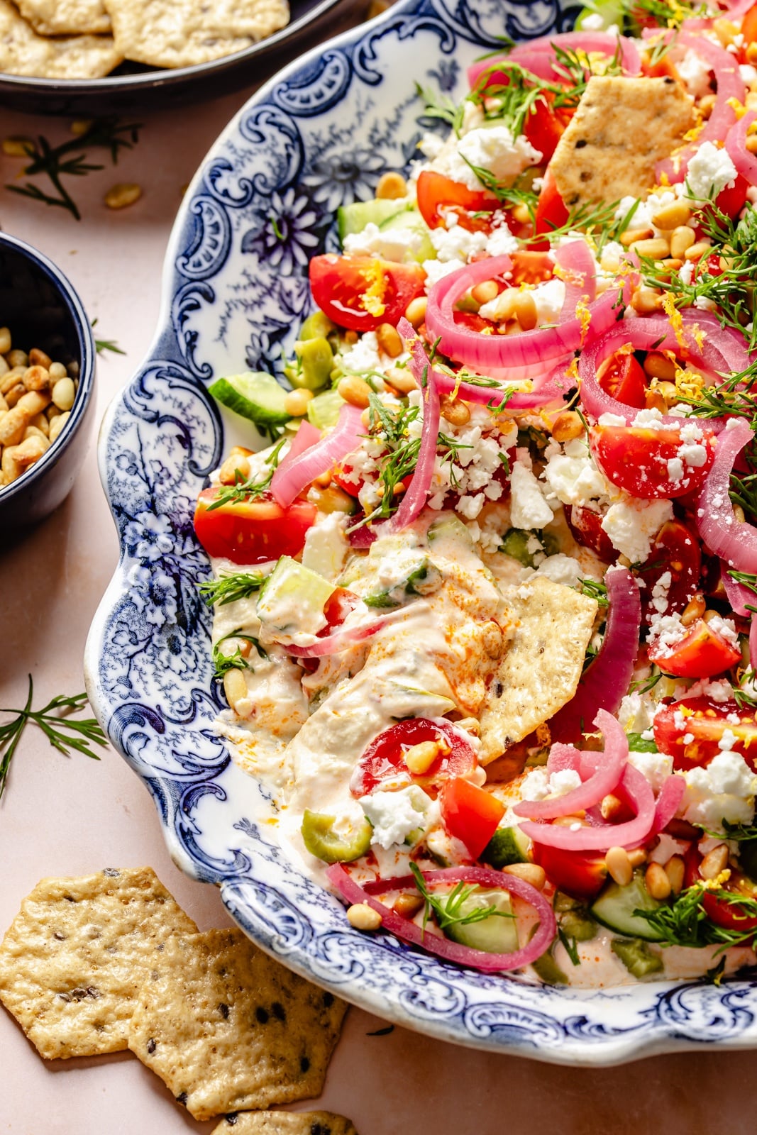 Easy, flavorful Mediterranean dip layered with hummus, creamy yogurt, and fresh toppings like olives, cucumber, and feta cheese. This savory party appetizer is a fun take on classic 7-layer dip and is delicious served with pita chips, pretzels, or naan bread! healthy layered mediterranean dip on a platter