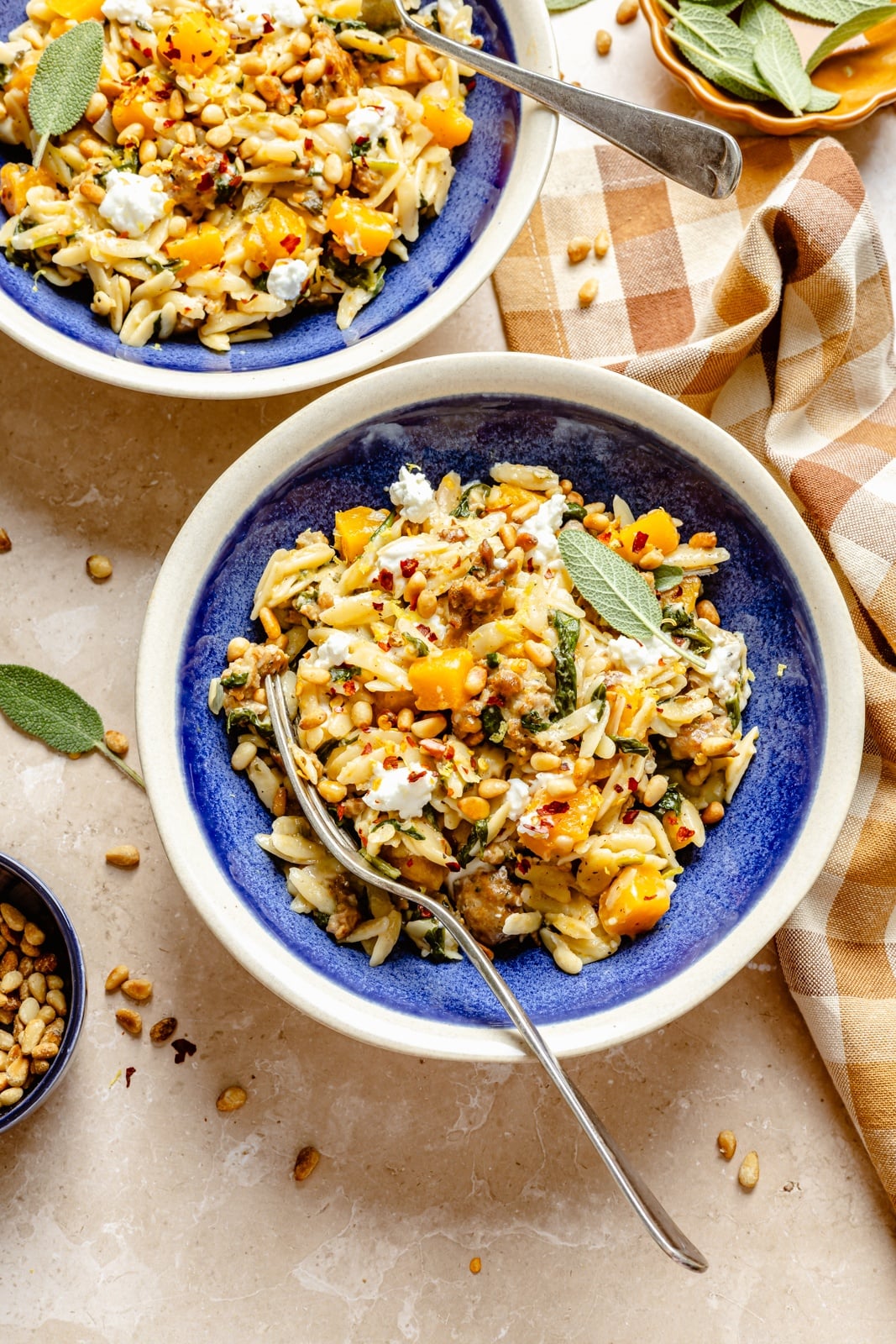 Creamy one pan butternut squash orzo with rich, sage-infused brown butter, spicy sausage, and tangy goat cheese. This sweet and savory orzo recipe is filled with cozy fall flavors, plus an extra boost of veggies from spinach! A beautiful weeknight dinner the whole family will love. butternut squash orzo with sausage in two bowls
