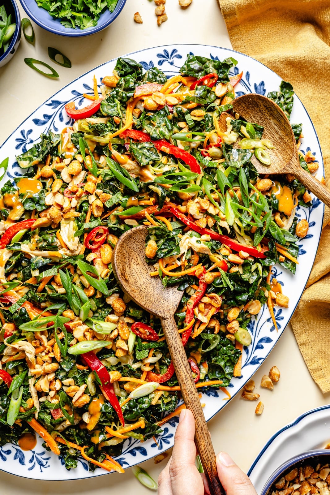 The ultimate crunchy peanut kale salad packed with a rainbow of vegetables and herbs, tossed in a dreamy, creamy ginger peanut dressing. This beautiful kale salad stays good in the fridge for days, making it the perfect high-fiber, protein-packed meal prep lunch! Enjoy as is or add an extra boost of protein for a heartier meal. peanut kale salad on a platter with wooden tongs
