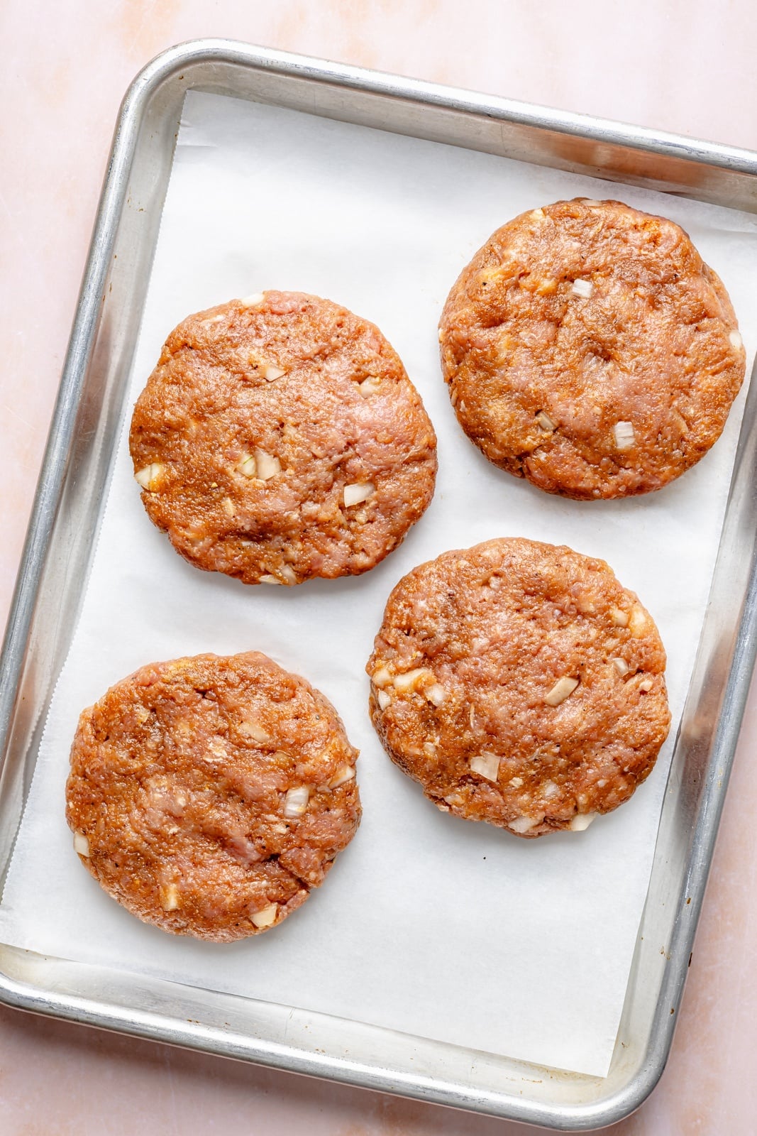 Flavorful, juicy BBQ bacon turkey burgers with a Hawaiian-inspired twist from a slice of sweet grilled pineapple. Use your favorite BBQ sauce, add a kick of heat from pepper jack cheese, and grill or pan-fry these burgers for the ultimate summer dinner! uncooked BBQ turkey burgers on a baking sheet