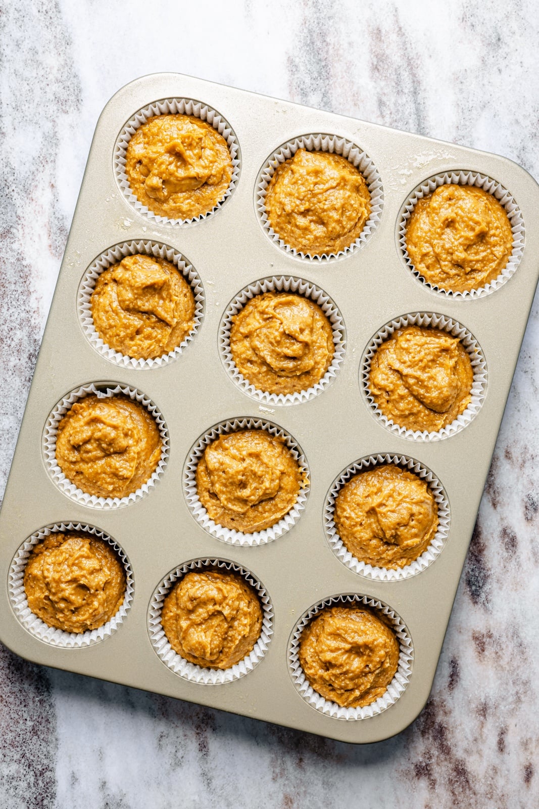 Fluffy butternut squash muffins infused with homemade chai spices, then topped with a simple salted honey glaze that truly takes these to the next level. These fall-inspired, freezer-friendly butternut squash muffins are easy to make and have hints of caramel flavor thanks to a touch of brown butter. Perfect with a cup of coffee! unbaked butternut squash muffins in a muffin tin